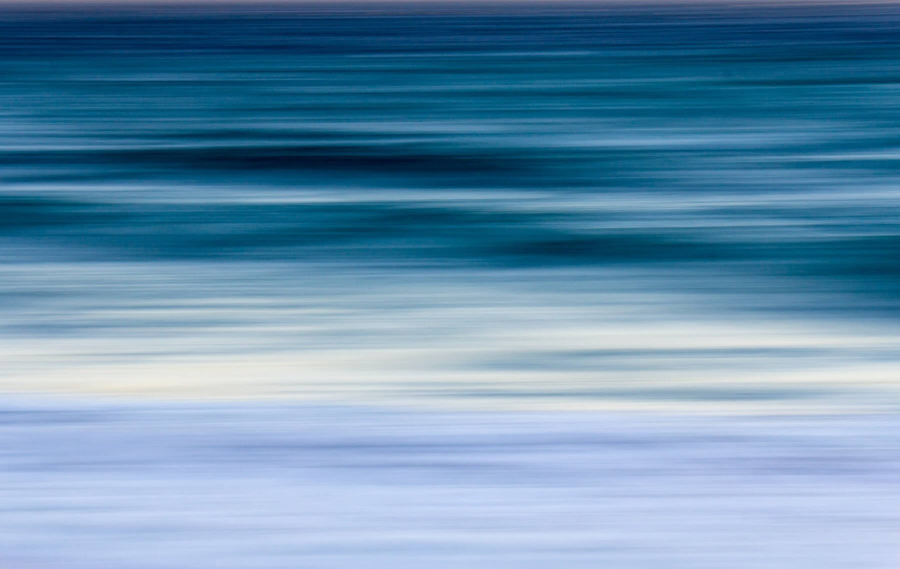 Fotografía abstracta de un océano con tonos azules y movimiento de las olas creando un efecto de barrido horizontal.